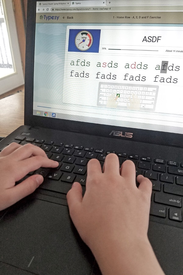 Child's hands typing on laptop with online typing lesson on screen