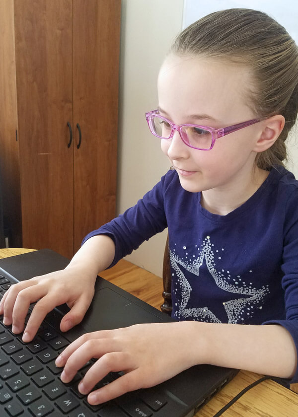 Smiling girl doing online typing lessons on laptop