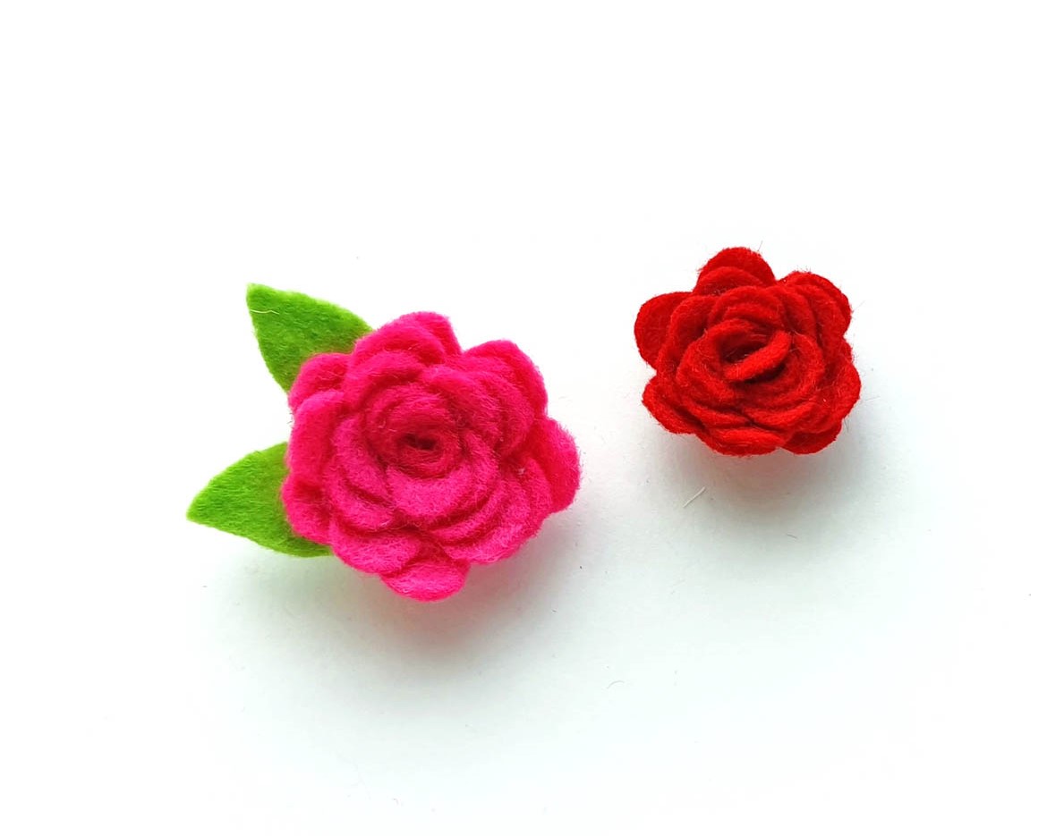 Image of a red felt rose and a bright pink felt rose with green leaves lying on a white background
