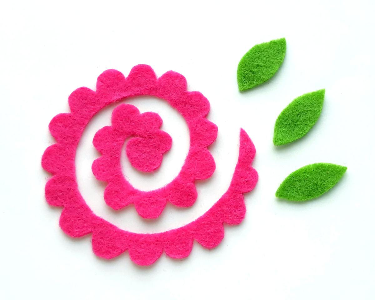 Image of a piece of bright pink felt cut into a spiral shape with 3 green felt leaves beside it