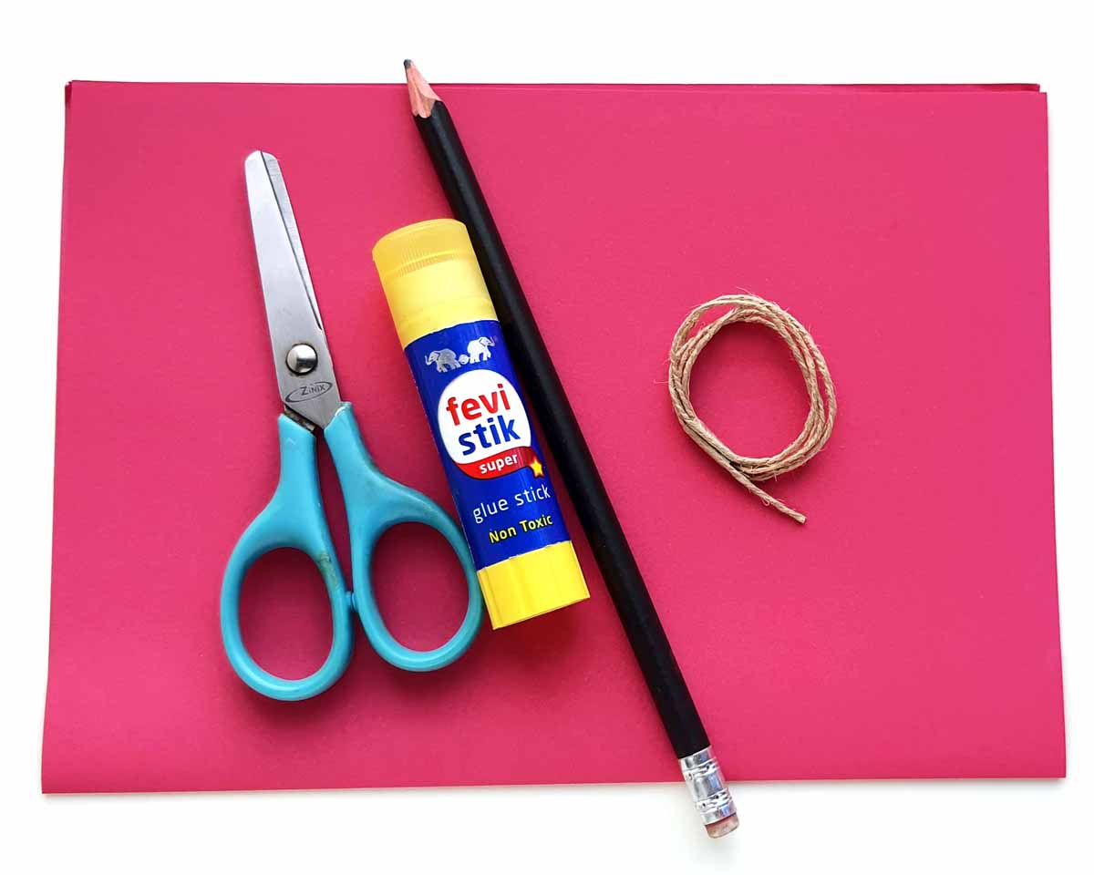 Image of a small pair of scissors, a glue stick, a black pencil, and a coiled piece of twin lying on red construction paper