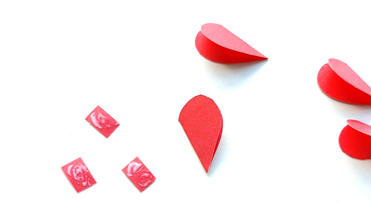Image of folded red paper hearts and small rectangles of red paper with glue on them