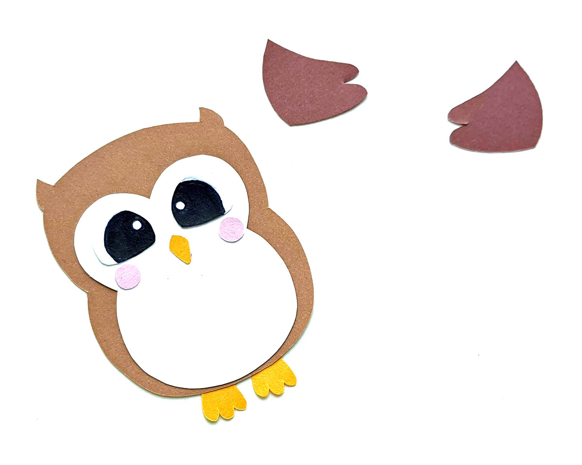 Partially made brown paper owl with several more paper pieces lying on a white background