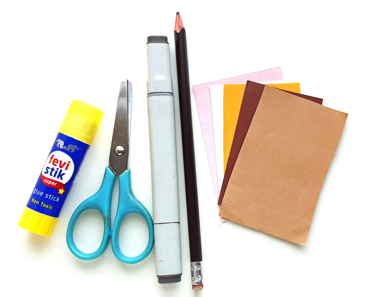 A glue stick, scissors, permanent marker, pencil, and pieces of colored paper lying on a white background