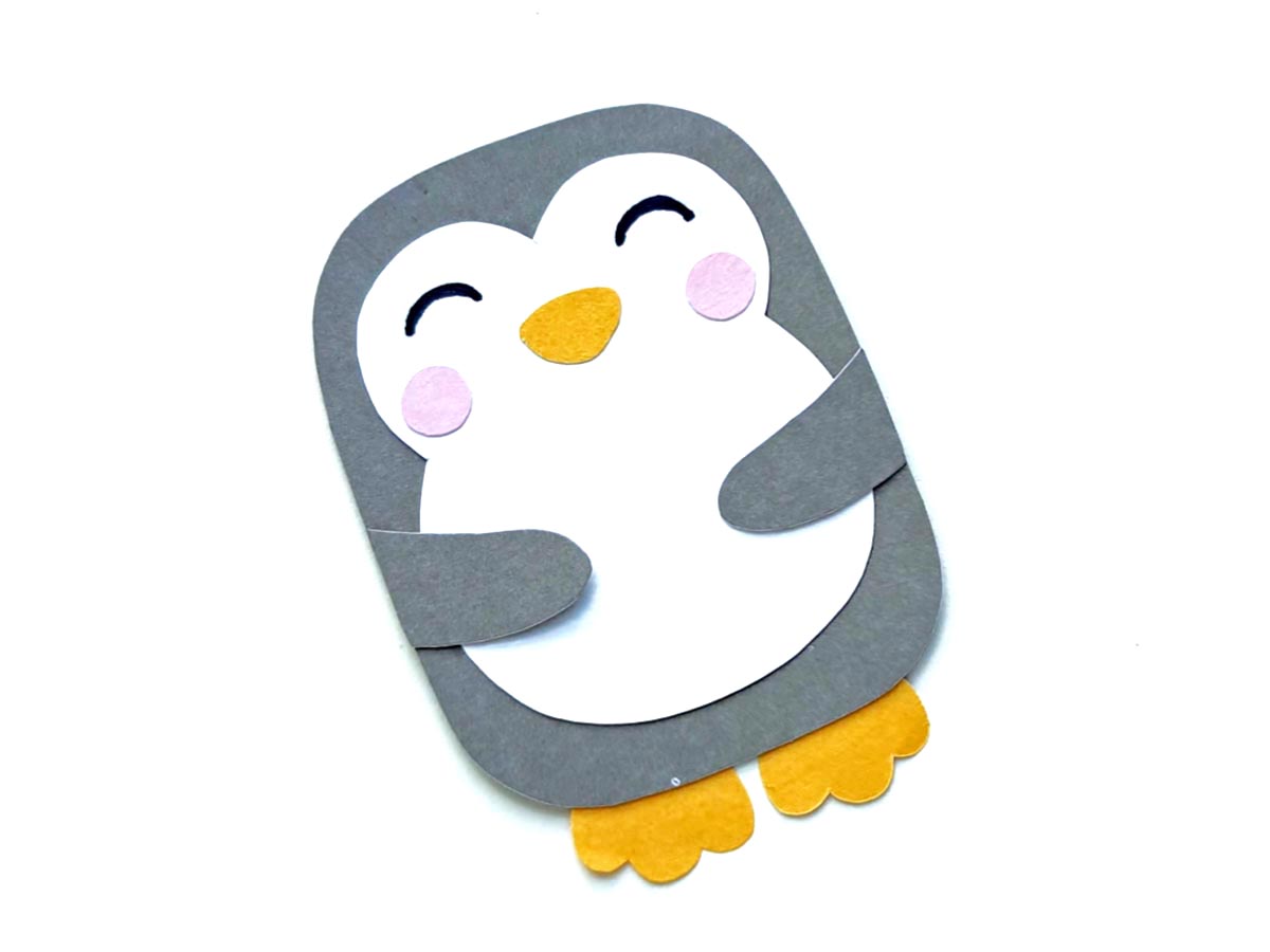 Image of gray and white paper craft penguin with orange feet and beak and pink blush circles on cheeks