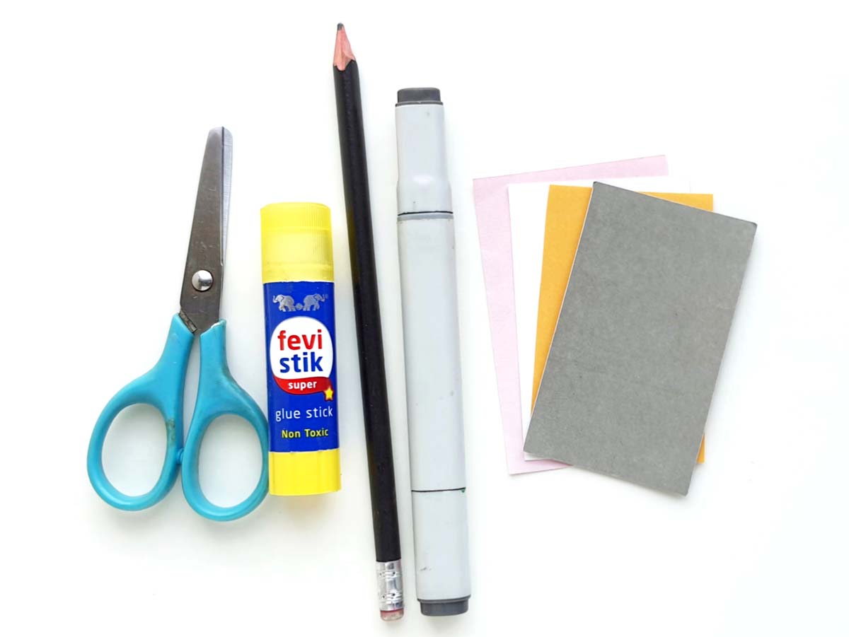 Image of a small pair of scissors, a glue stick, a pencil, a marker and several sheets of colored paper lying on a white background