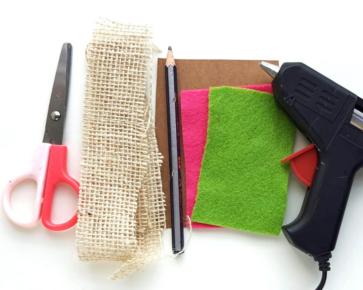 Image of scissors, burlap lace, colorful pieces of felt, and a black hot glue gun lying on a white background
