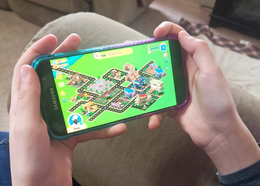 Image of child's hands holding a phone with a science game on the screen.