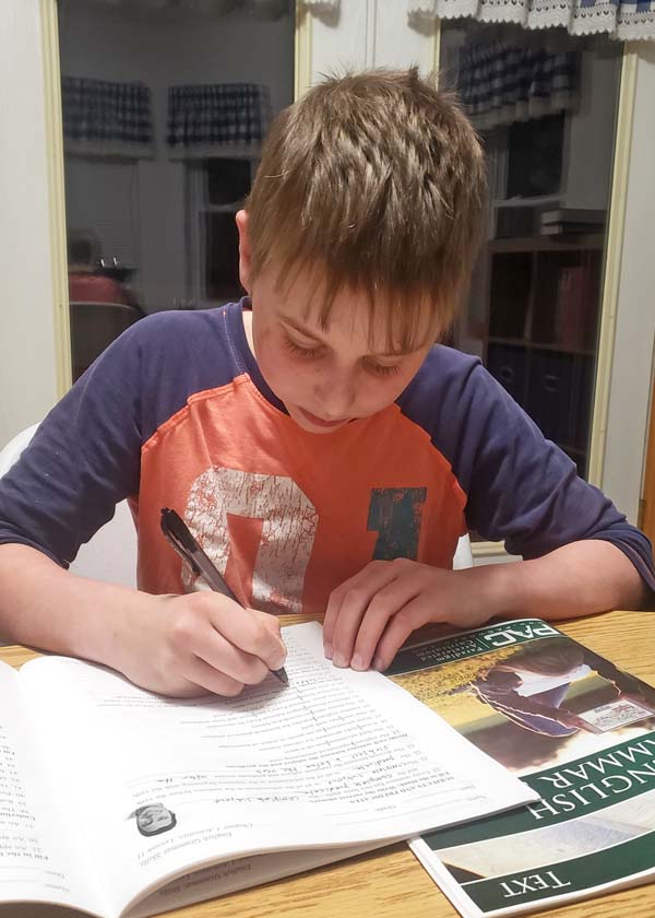 Image of teenage boy in orange and blue shirt, sitting at a table and writing in a workbook