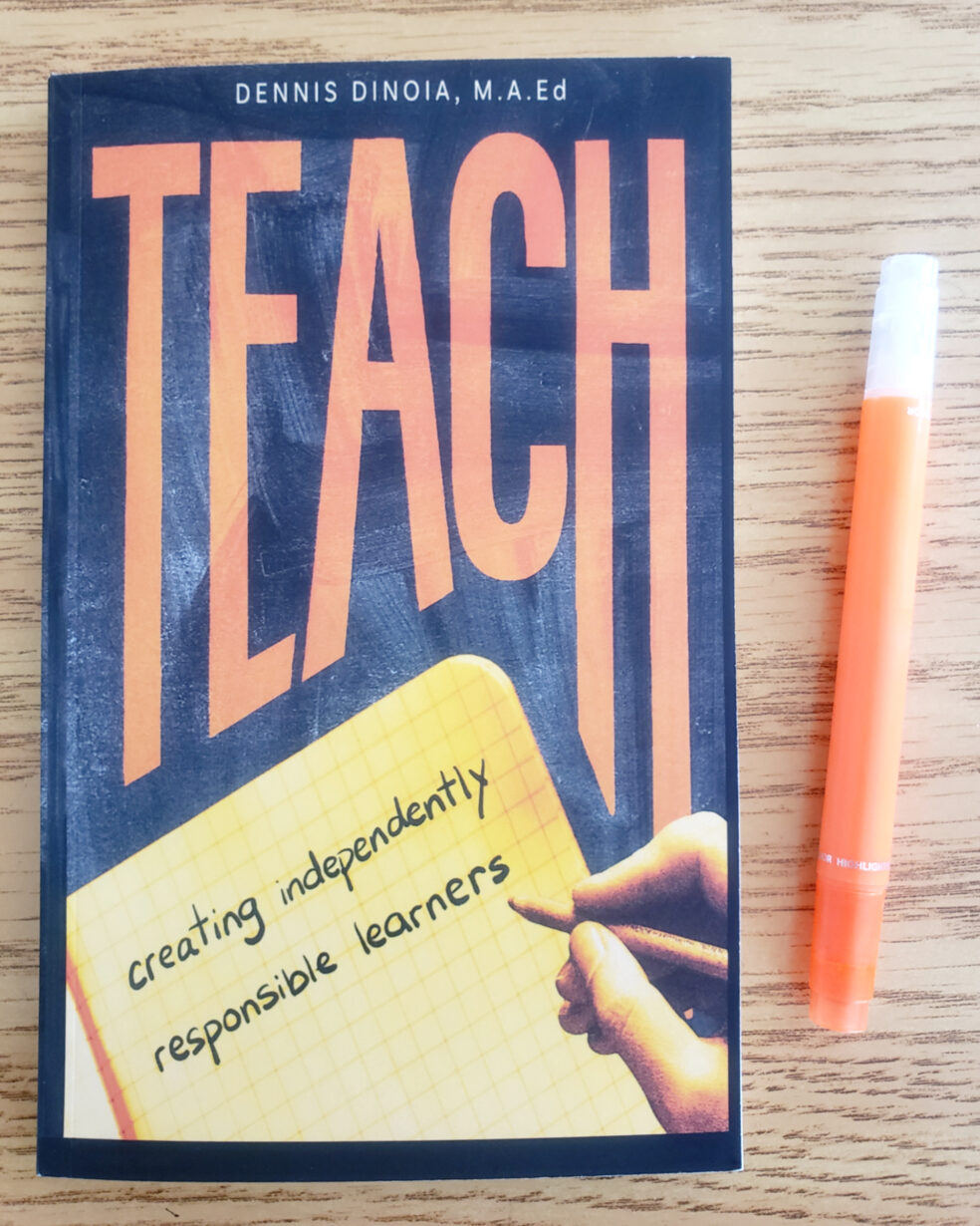 Photo of  the book TEACH by Dennis Dinoia lying on a wooden table with an orange highlighter lying beside it