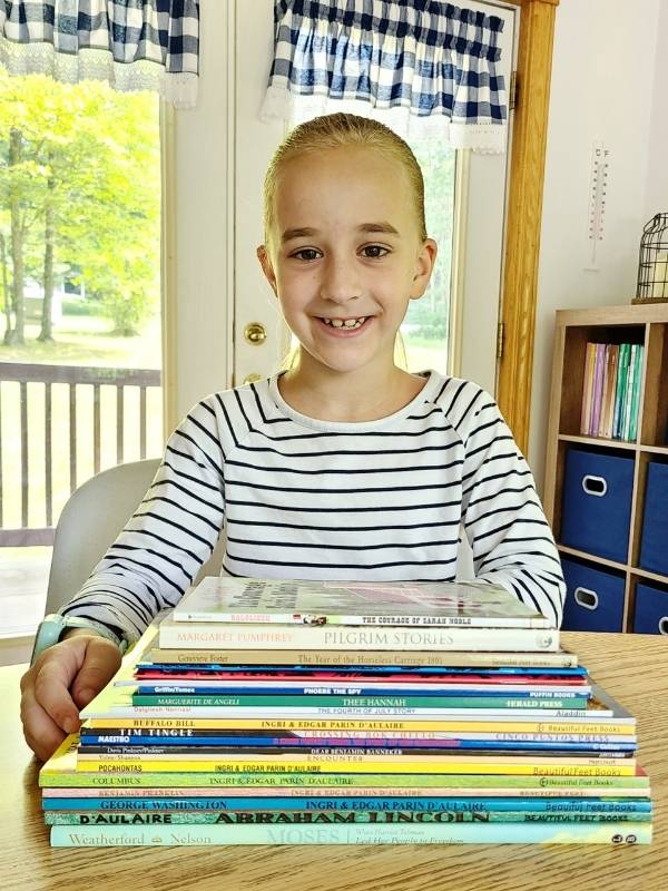 Image of smiling girl sitting at table with a stack of history books in front of her