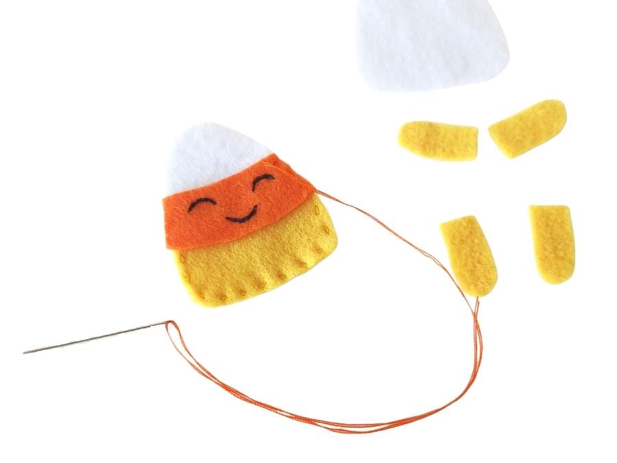 Image of yellow, orange, and white felt being sewed with orange thread to make felt candy corn.