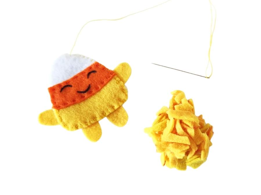 Image of yellow, orange, and white felt candy corn plush and a ball of yellow felt scraps on white background.