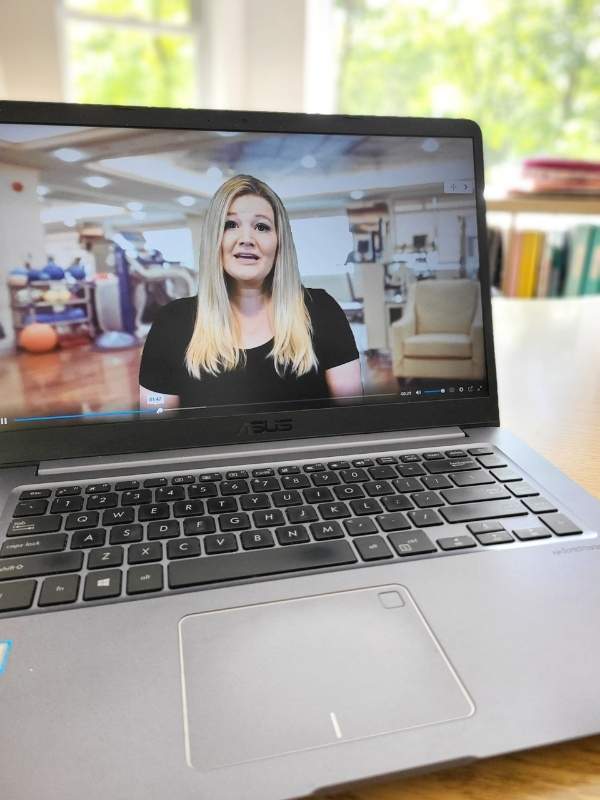 Image of laptop with screen showing video of woman in black shirt teaching.