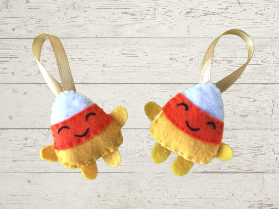 Image of 2 orange, yellow, and white felt candy corn ornaments on a wooden background.
