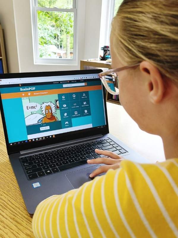 Image of middle school-aged girl homeschooling online. She is watching a video about Einstein on a laptop.