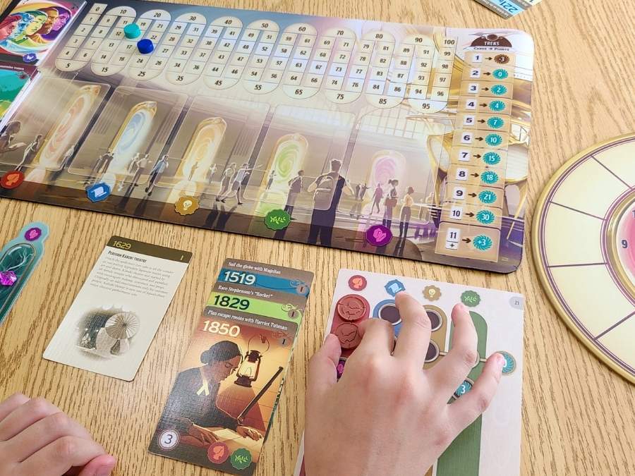 Image of young girl's hand moving playing pieces on a game board, with history cards laid out beside her
