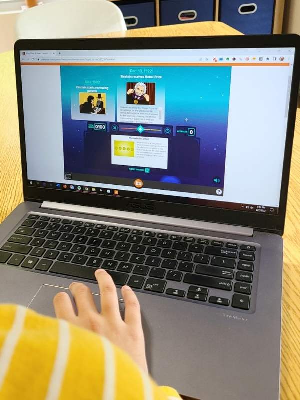 Close-up image of laptop with educational game on the screen and a girl's fingers touching the mousepad