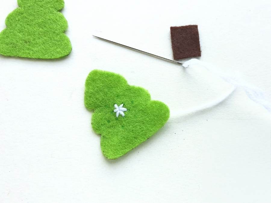 Image of green felt Christmas tree cutout and a needle filled with white embroidery floss.