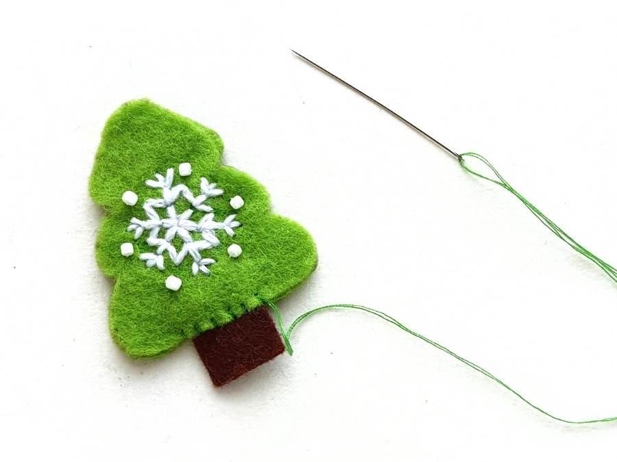 Image of green felt Christmas tree with brown felt trunk being sewed together with green thread.