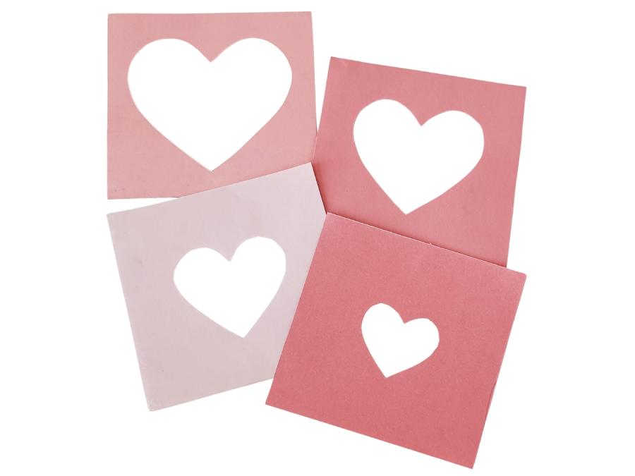 Image of 4 pink squares of paper with various sizes of hearts cut out of the center.