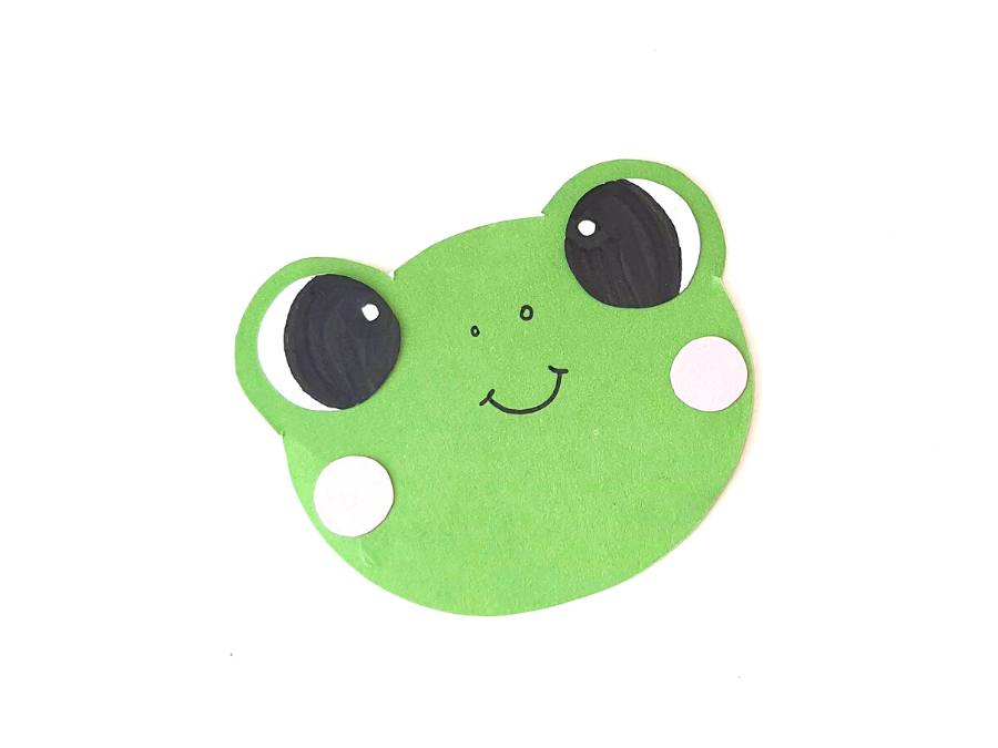 Image of green paper frog face with pink blush on cheeks and large eyes, all on a white background.