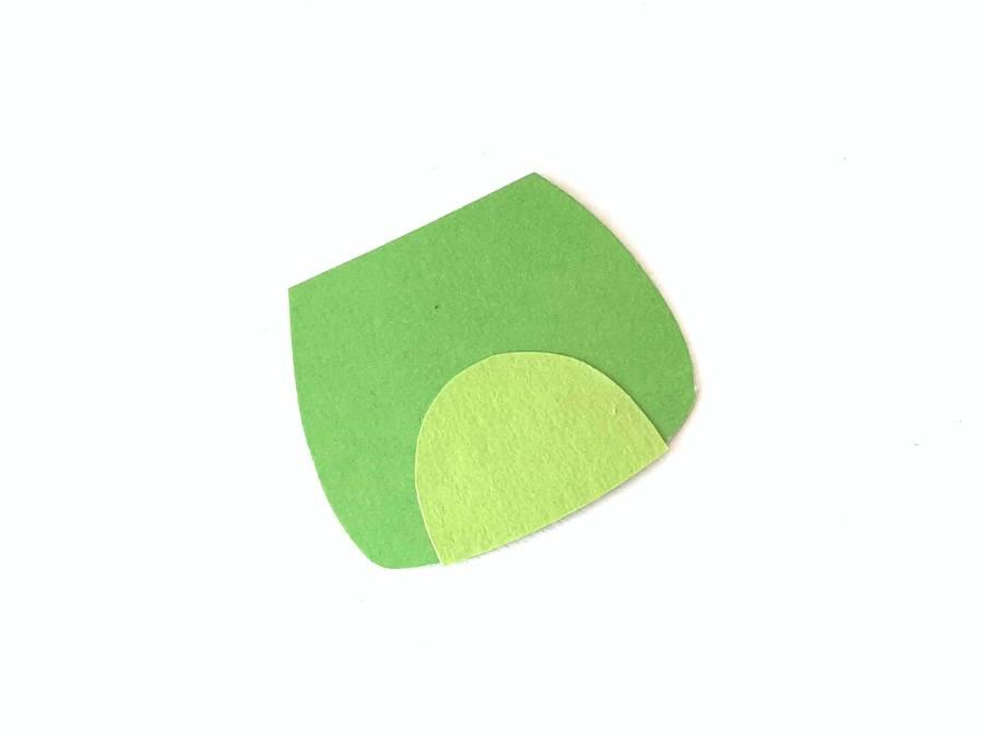 Image of green construction paper cut out in the shape of a frog's body, on a white background.