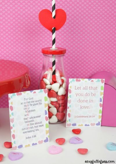 Image of two printable valentine cards surrounded by candy conversation hearts, with a jar of red and white heart candies in front of a pink background.