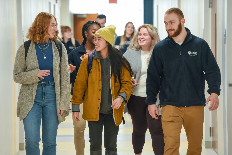 Image of group of Thiel College students smiling and talking as they walk down a hallway together.