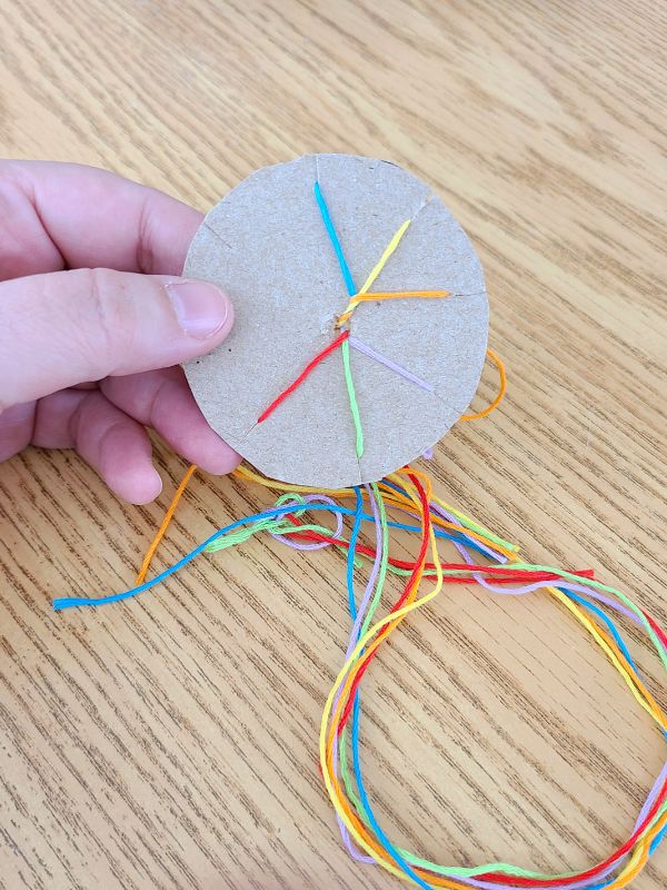 Image of a small handmade cardboard loom with brightly colored embroidery floss wound around.
