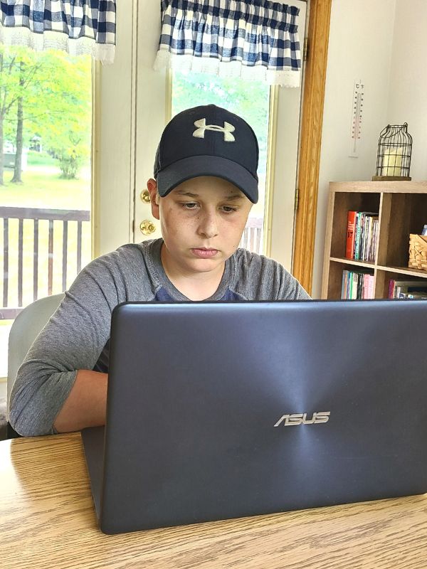 Image of teenage boy in blue ball cap doing homeschool job skills training on a laptop.