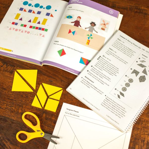 Image of a Singapore math textbook and a set of yellow tangrams on a wood table.
