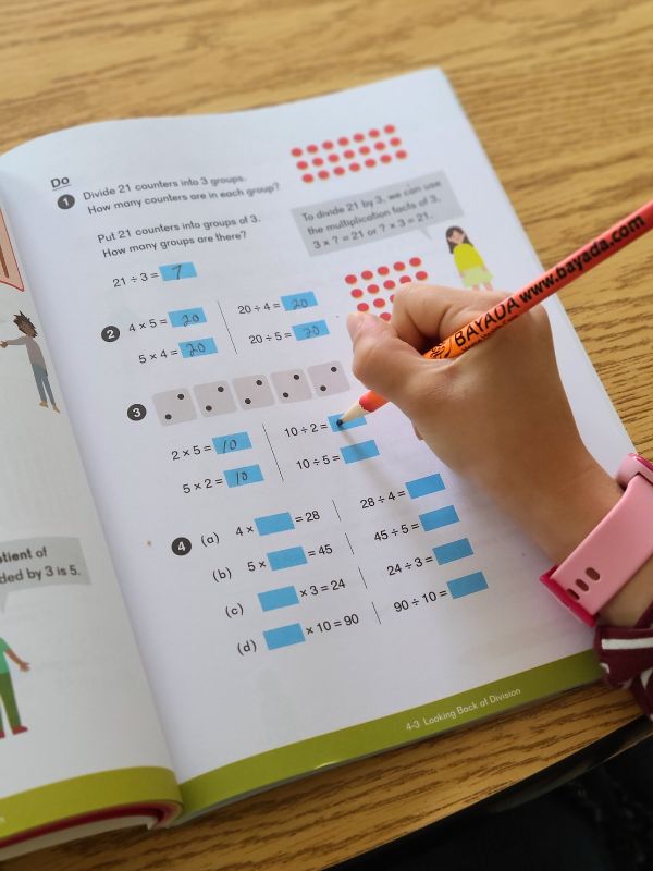 Image of a young girl's hand holding a pencil and writing in a Dimensions Math book.