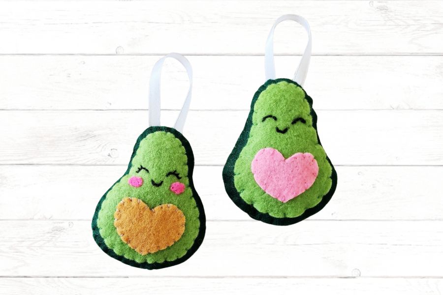 Felt avocado tutorial Image of two felt avocado stuffies lying on a light wood background.