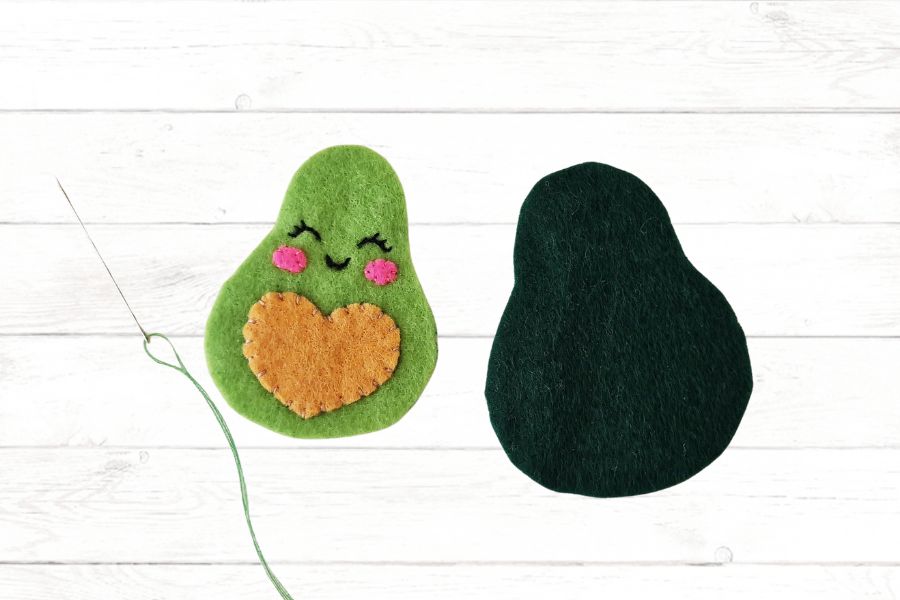 How to make an avocado stuffie Image of felt pieces lying on a light wooden background to be stitched together.